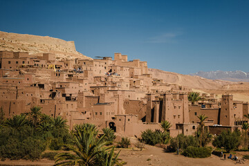 Traditional earthen village built on a hillside with palm trees in a dry valley, adobe architecture in arid mountains, historic rural settlement, desert landscape and cultural heritage.