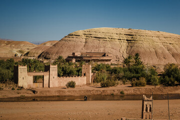 Traditional earthen village in southern Morocco with adobe architecture, palm trees and desert valley landscape, historic rural settlement in arid environment.