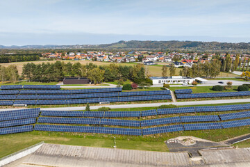 Obraz premium Aerial view shows solar panels arranged on land near water with houses and trees in the background on a clear day.