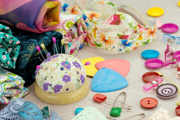 Sewing and craft accessories. A pin cushion, drawing ruler, fabric, buttons, and pins are scattered on the table.