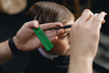 Young caucasian boy getting haircut close-up of hair styling in salon retro barbershop, top view