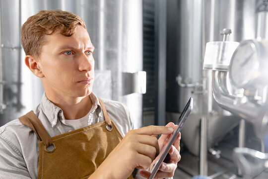 Caucasian male adult brewer monitoring equipment in modern brewery facility with tablet computer - Powered by Adobe