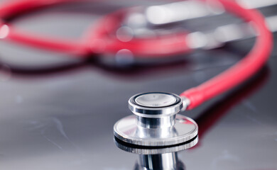 Closeup of red stethoscope on reflective surface, medical concept