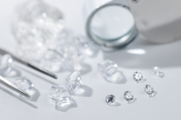 Closeup of loose diamonds and jeweler's tools on white surface