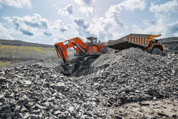 Obraz premium Expansive open pit coal mine with excavator and yellow dump truck on rocky terrain