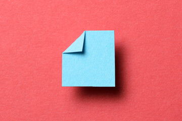 Light blue blank paper note cardboard with folded corner dog-ear earmark, shadow and copy space for text on red background