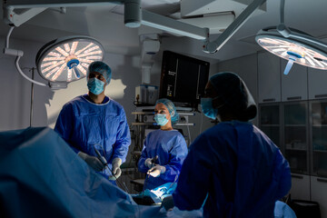 Team of surgeons in a dark operating room performing a complex laparoscopic procedure under bright surgical lights, using specialized medical monitors and minimally invasive instruments in a clinic.