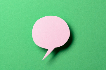 Pink cut out paper speech bubble with shadow and copy space for text on green background, close-up...