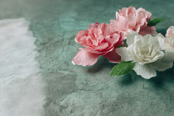 Handmade mulberry paper flower with delicate petals in soft pink and white colors arranged on textured green background creating gentle and artistic atmosphere