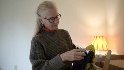 Mature woman unpacks an antique camera, reminiscing about family memories connected to this cherished heirloom and its history.