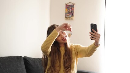 A young woman sits on her sofa in her new home, beaming as she holds up the key during a video call. Her excitement captures the joy of sharing this milestone with loved ones.