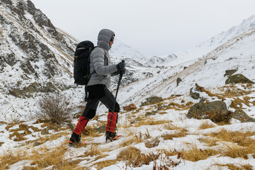 Hiker walking uphill in snowy mountain landscape with backpack and trekking poles. Winter trekking...