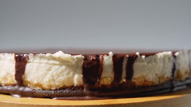 A chocolate-glazed cheesecake slowly rotates, revealing a creamy filling and sponge base. Minimal studio lighting highlights the texture and quality of the handcrafted dessert.