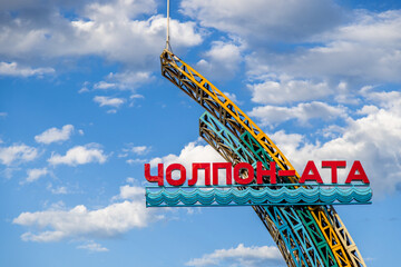 Large metal structure with welcoming sign to Cholpon-Ata town on Issyk-Kul lake in Kyrgyzstan on sunny day.