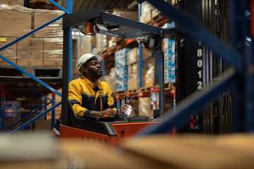 Fototapeta premium Warehouse worker man african american operating forklift while using walkie-talkie for communication, ensuring safety, efficiency in logistics, shipping, inventory control in industrial environment.