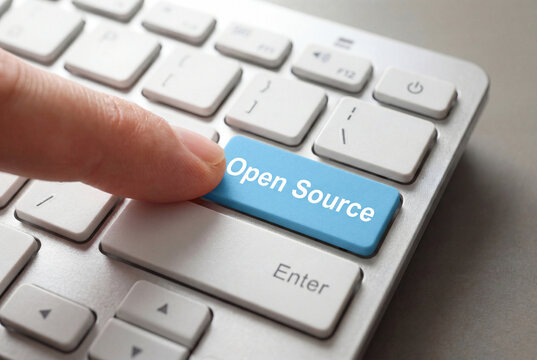 A finger pressing a blue OPEN SOURCE key on a modern laptop keyboard. Concept of software freedom, community development, and transparent digital innovation.