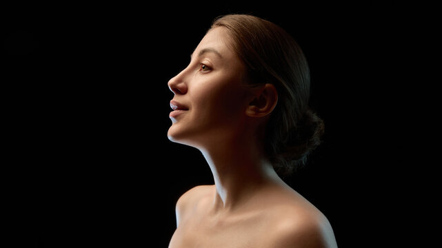Low key female profile portrait with soft rim lighting. Concept of self perception, body confidence, real appearance and use in campaigns promoting honest beauty and inclusive representation.