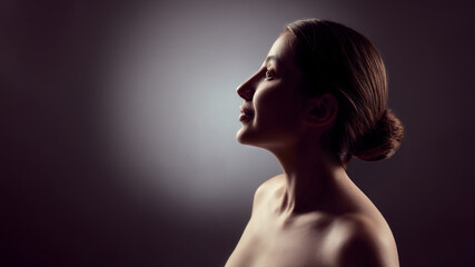 Side profile portrait of young woman in low light studio environment. Concept of body acceptance,...