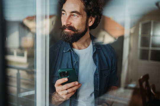 Man holding phone contemplating looking out window
