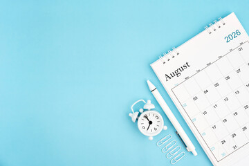 Fototapeta premium August 2026, Monthly desk calendar for 2026 year and alarm clock with paper clips on blue color background.