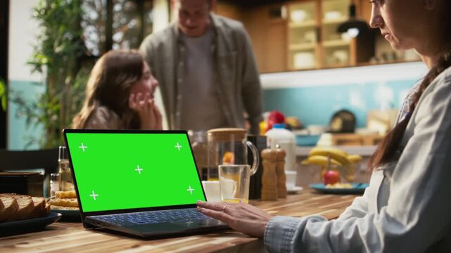 Green screen laptop next to family enjoying relaxing weekend breakfast, parents serving toast and juice while pre-teen girl eating pastry. Cozy atmosphere reflects togetherness. Camera A.