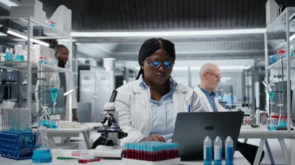 Female researcher brainstorms in laboratory, using laptop software, driving treatment discovery. African american woman thinking, using bioinformatics application on notebook in sterile lab, camera A - Powered by Adobe
