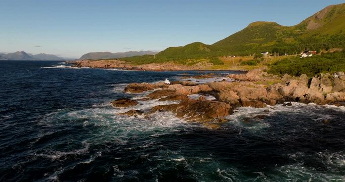 Aerial pullback orbit of rugged coastline and blue sea near Uvaershula Stokmarknes Norway, waves crashing on rocks