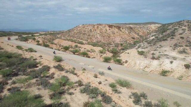 Aerial view of motorbike and truck crossing on dirt road, desert hills