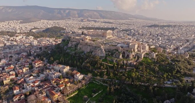 Cinematic forward-moving drone shot from the Ancient Agora toward the Acropolis at sunset in Athens, Greece. Golden light, ancient ruins, and historic skyline create an epic scene for travel etc.