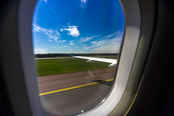Airplane window view of runway and green field.