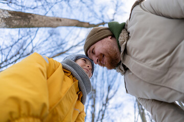 In a serene winter forest, a son and father have a great time, both dressed in warm clothes. The scene captures a moment of love against a snowy backdrop, evoking warmth and connection. Father's Day