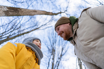 In a serene winter forest, a son and father have a great time, both dressed in warm clothes. The scene captures a moment of love against a snowy backdrop, evoking warmth and connection. Father's Day