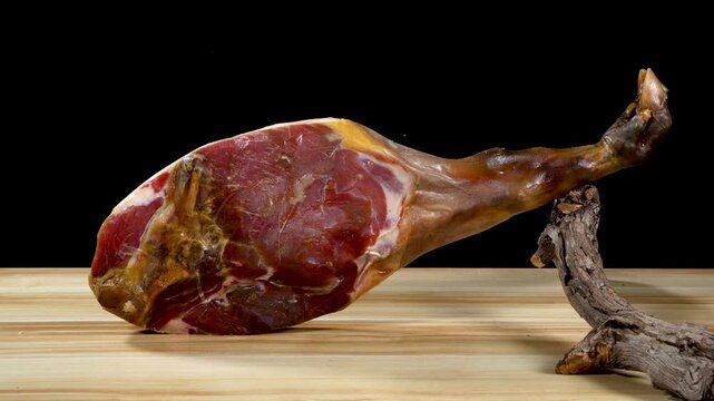 Whole Cured Spanish Jamon Ham Leg On Wooden Board Against Black Background