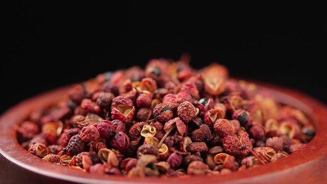 Dried Sichuan Peppercorn in a Brown Wooden Bowl Rotating Slowly on a Black Background.