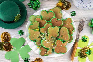 Shamrock shaped green tasty sweet pancakes for St Patricks day breakfast. Creative homemade tasty fried pan cakes with sugar sprinkles and Saint Patrick holiday decor