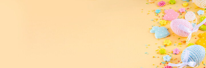 Cute and bright pastel colored Easter eggs and bunny background. Pink. blue, yellow colored bunny rabbits, eggs and flowers sugar sprinkles on light yellow background