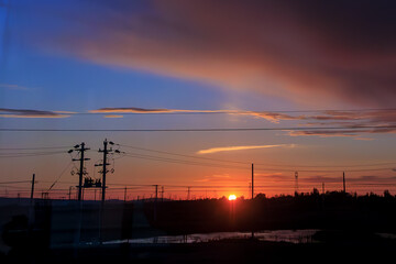 Stunning sunset with vibrant orange and pink hues illuminates sky, silhouetting power lines and poles against horizon. serene landscape evokes sense of calm and tranquility
