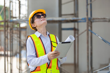 Confident female engineer in safety gear inspecting construction site with tablet and blueprints, symbolizing leadership, quality control, modern infrastructure development.