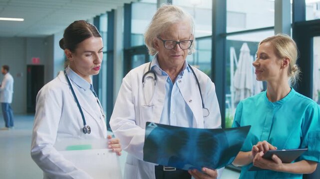 Three medical professionals reviewing chest X-ray together in bright hospital corridor. Senior doctor holding image while younger colleagues discuss. Team collaborating and evaluating condition.