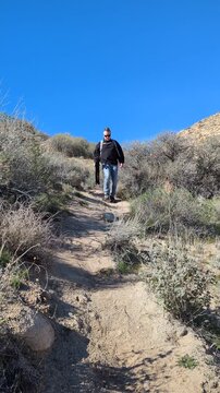 Hiker with backpack and tripod hiking down a desert dirt trail