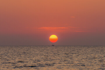 The sun begins to set and the silhouette of a fishing boat.