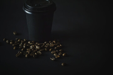 Black paper cup and coffee beans on dark background.