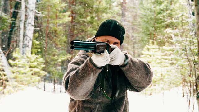 A real hunter with a gun takes aim and prepares to shoot. The hunter tracks down wild forest animals and hunts them. Winter hunting.