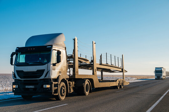 An empty car transporter drives along the highway against a blue sky