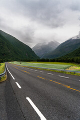 Norwegian National Road 70 stretches through Sunndalen Valley in M&oslash;re og Romsdal. Dark dramatic clouds cover the sky above the mountains and green fields along the route