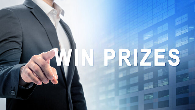 Businessman in a suit touches a digital screen with the text "Win Prizes" displayed. The background feature of a modern glass building. Concept of online contest, giveaway, raffle, or lottery - Powered by Adobe