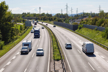 Cars and trucks move along a busy highway during daylight, highlighting transportation links between cities and urban areas.
