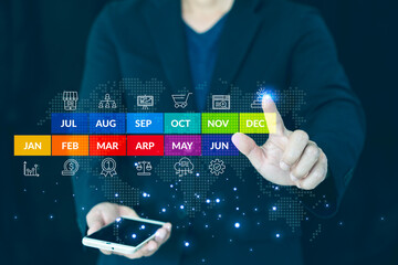 Business growth concept showing a businessman holding a smartphone and interacting with a futuristic virtual screen. The interface displays a colorful yearly calendar from January to December 