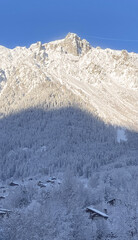 Sunlit alpine mountain peaks above snowy forest and village in winter