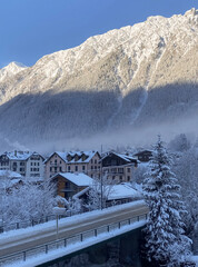 Snowy alpine town with bridge beneath sunlit mountain ridge